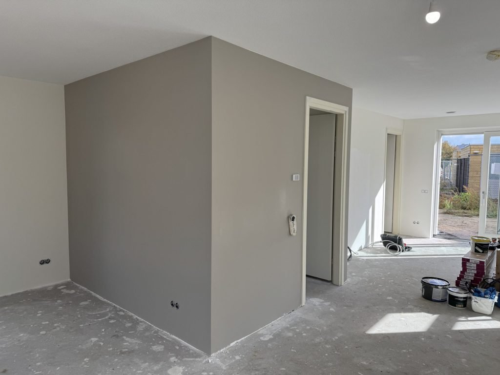 Nieuwbouwwoning met een pas gesausde grijze wand en verfemmers op de vloer